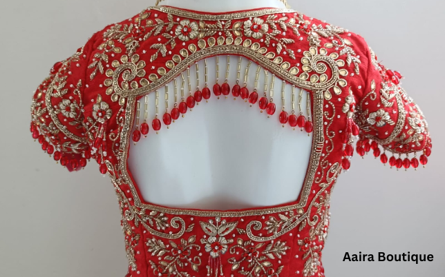 Close-up of a red Indian ethnic wear blouse with intricate gold and silver hand embroidery and red beaded tassels on the back cut-out, displayed on a mannequin.